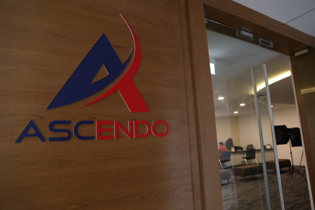 The Ascendo logo mounted on a wood-panelled wall beside a glass door into an office.